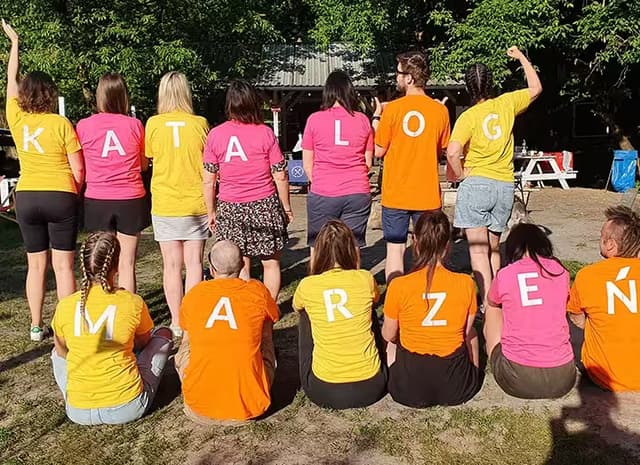 grupa osób odwróconych plecami w kolorowych koszulkach, którzy tworzą napis katalog marzeń