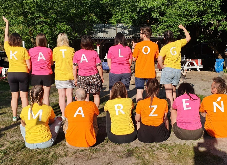 grupa osób odwróconych plecami w kolorowych koszulkach, którzy tworzą napis katalog marzeń