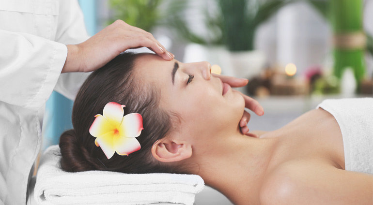 Kobieta z kwiatem we włosach podczas masażu twarzy.