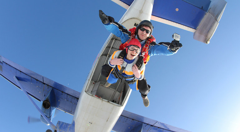 Uśmiechnięta dziewczyna wyskakuje ze spadochronem z samolotu