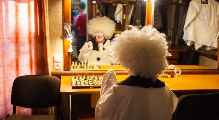 Aktor w teatrze z białą peruka przeglądający się w lustrze