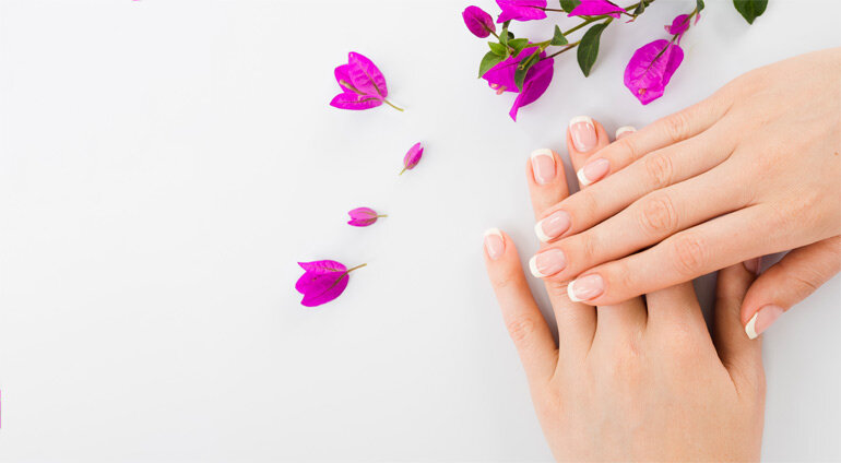 jasny manicure francuski na dłoniach obok kwiaty