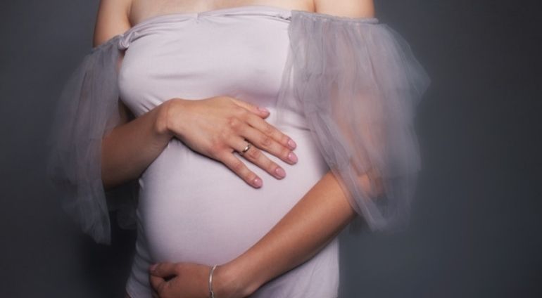 Kobieta w białej sukience na sesji fotogranicznej w ciąży