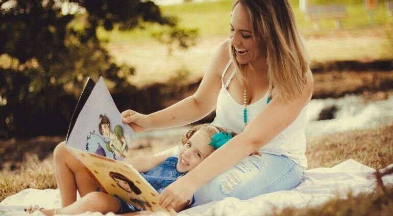 Uśmiechnięta mama czyta książkę z dzieckiem w parku