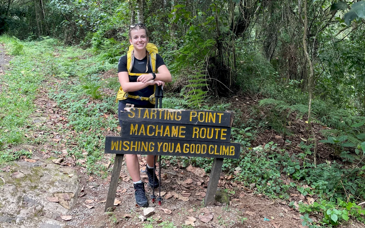Dziewczyna uśmiecha się przy znaku na starcie trekkingu na Kilimandżaro